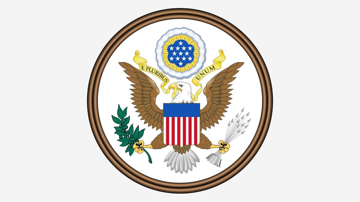 The front of the Great Seal of the United States: a bald eagle with a red, white and blue shield on its breast, an olive branch and thirteen arrows in its talons, and a scroll reading E Pluribus Unum